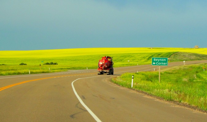 Red truck on an open road with a green field in the countryside