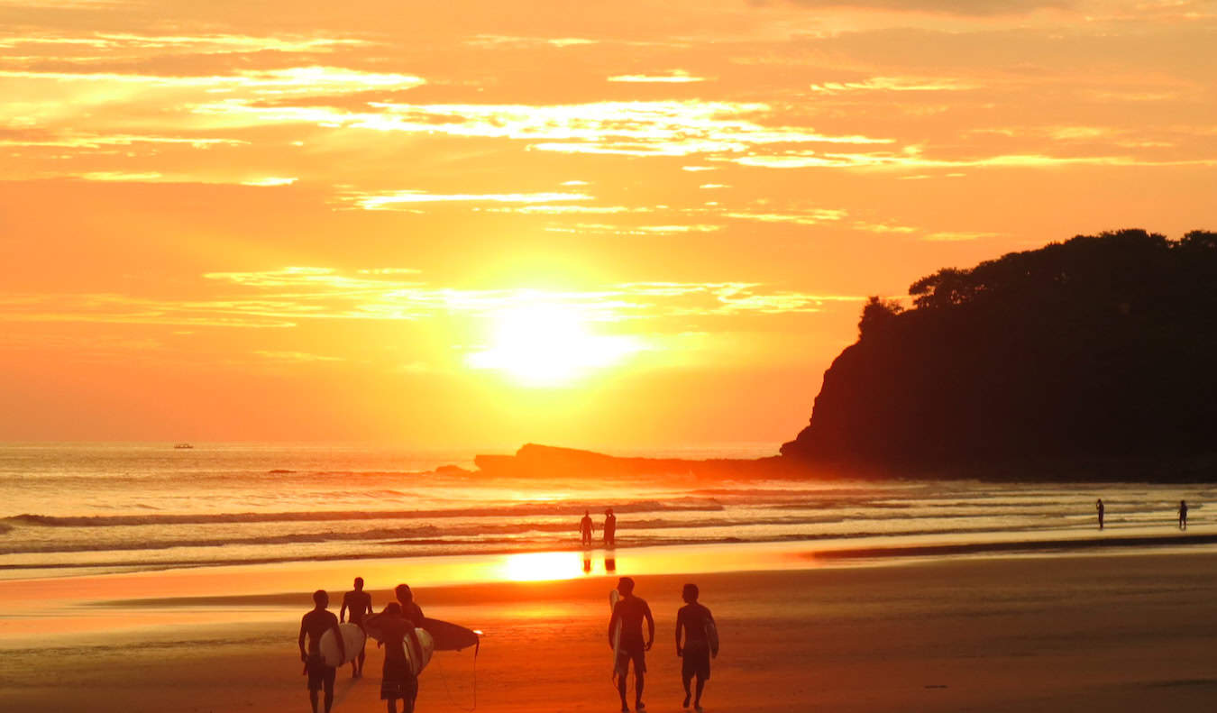 An epic golden sunset on the coast of San Juan del Sur in Nicaragua with a surfer in the distance