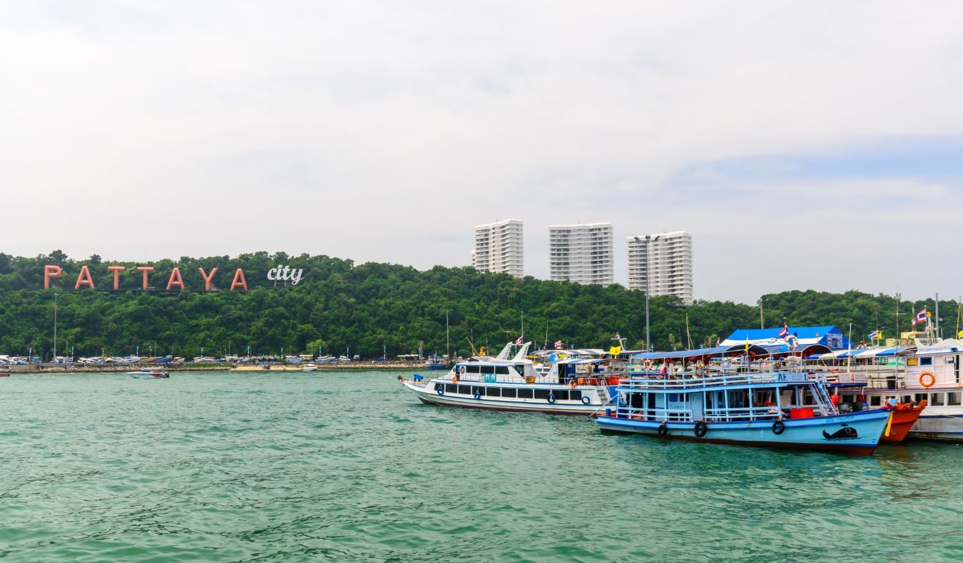 Small ferries parked in the water in front of a large sign on the shoreline trees that says 'PATTAYA' in Pattaya, Thailand