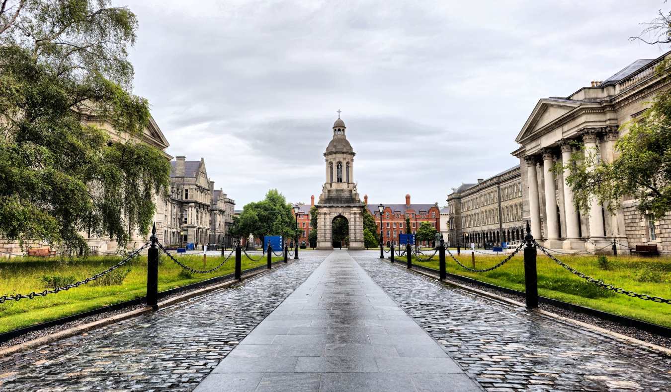 A cobblestone pathway flanked by historic buildings at Trinity College on a rainy day in Dublin, Ireland