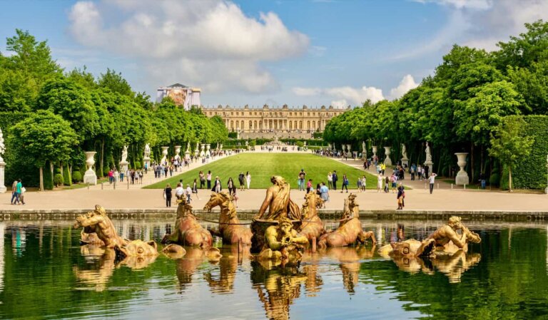 The statues and beautiful facade of the Palace of Versailles in France with people exploring the grounds in the distance